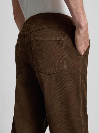 Męski model nosi brązowe, bawełniane spodnie Stoffhose mit elastischem Bund od Pegador, tekstura sztruksowa, tylna perspektywa z bliska.