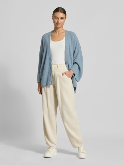 Frauenmodel trägt Relaxed Fit Cardigan mit Woll-Anteil Modell 'Damsville' von American Vintage in Hellblau, Strick-Optik, Ganzkörperansicht von vorne. Elastischer Material-Mix, V-Ausschnitt, Knopfleiste, Rückenlänge 68 cm, Ärmellänge 37 cm.