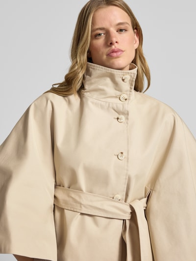 Frauenmodel trägt Trenchjacke mit Stehkragen Modell 'Isa' von Gina Tricot, beigefarbener Baumwoll-Mix, Taillierter Schnitt, Nahaufnahme Oberkörper.