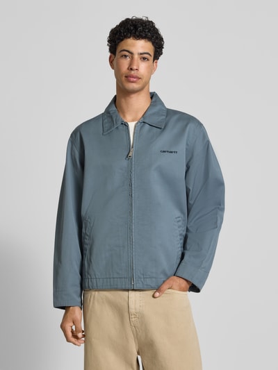 Männermodel trägt Jacke mit Label-Stitching und Eingrifftaschen von Carhartt Work In Progress in Blau, Reißverschluss, Umlegekragen, Regular Fit, Nahaufnahme Oberkörper.