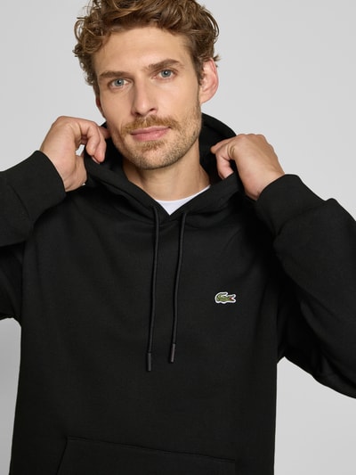 Mannelijk model draagt zwarte Relaxed Fit Hoodie aus Baumwoll-Mix van Lacoste, Heren sweatshirt, Nahaufnahme bovenlichaam.