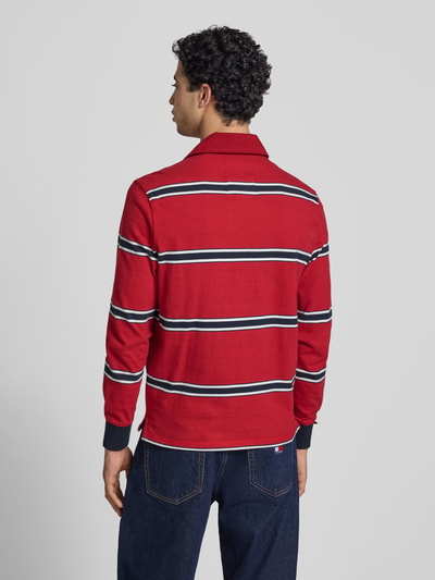 Männermodel trägt Regular Fit Poloshirt mit Logo-Stitching von Superdry in Rot mit weißen und dunkelblauen Streifen, Rückenansicht, Ganzkörperansicht Rückansicht.