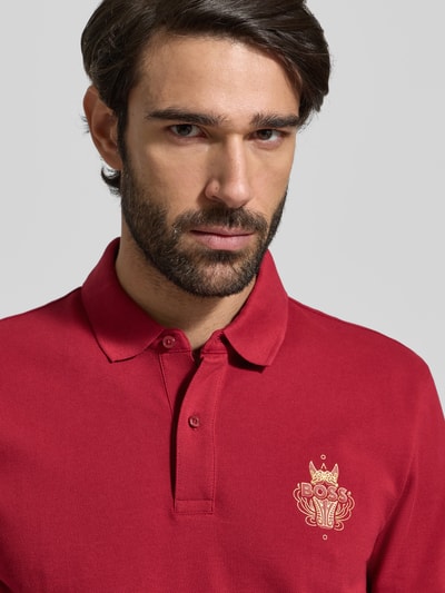 Männermodel trägt Regular Fit Poloshirt aus reiner Baumwolle Modell 'QIANG' von BOSS, Optik: Unifarben, Motiv-Label-Print, Nahaufnahme Oberkörper.