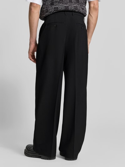 Mannmodel draagt Relaxed Fit stoffen broek uit wolmix van Filippa K, zwart, bandplooien, gulp- en achterzakken, geheel van achteren.