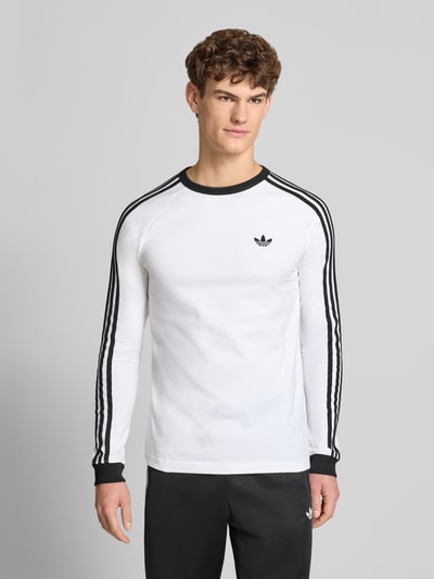 Männermodel trägt Longsleeve mit Label-Stitching von adidas Originals in Weiß mit schwarzen Details, reine Baumwolle, Nahaufnahme Oberkörper.