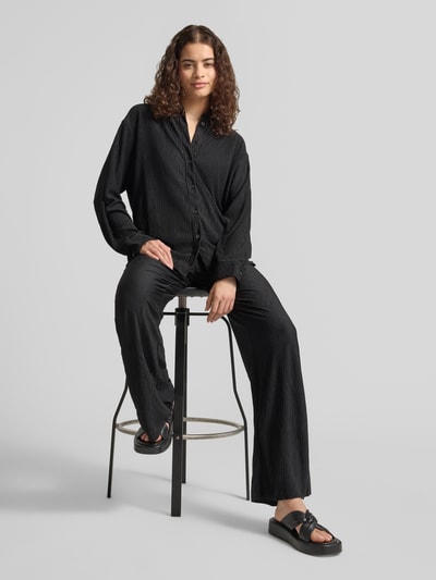 Frauenmodel trägt schwarze Flared Cut Hose mit Plisseefalten und elastischem Bund von REVIEW, Material-Mix mit Stretch-Anteil, Ganzkörperansicht von vorne.