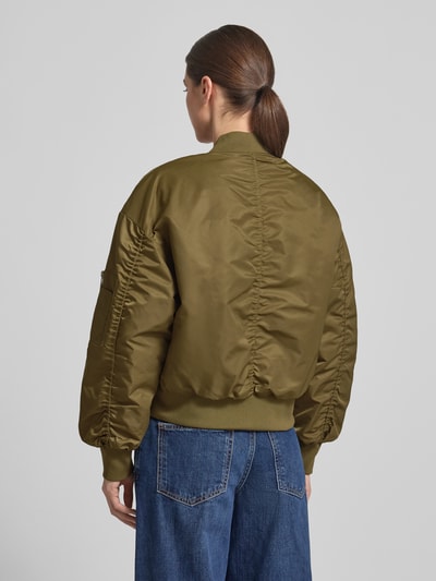 Vrouwenmodel draagt Regular Fit Bomberjacke met Stehkragen Modell 'Helga' van My Essential Wardrobe in olijfgroen, elastische boorden, zakken, detailzak op mouw, gladde textuur, ruglengte 54 cm, schouderbreedte 56 cm, borstwijdte 58 cm, mouwlengte 53 cm, totaalbeeld achteraan.