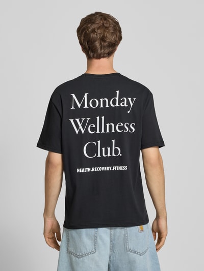 Mężczyzna nosi Relaxed Fit T-Shirt aus reiner Baumwolle Modell 'CAP' od ONLY & SONS, czarne z białym nadrukiem, widok całej sylwetki od tyłu.
