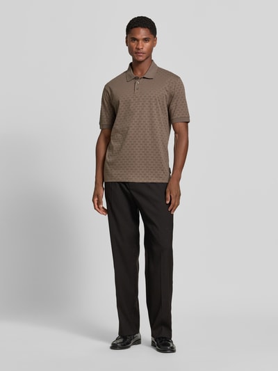 Männermodel trägt Regular Fit Poloshirt aus reiner Baumwolle von Armani Exchange mit Allover-Logo-Print, braun, Ganzkörperansicht von vorne.
