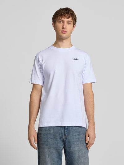 Mężczyznęmodel nosi męski t-shirt z bawełny o prostym kroju, wyhaftowane logo, biała gładka struktura, model 'ACCIANO CLASSIC' od Ellesse, długość tyłu w rozmiarze M: 67 cm, zdjęcie całej sylwetki z przodu.