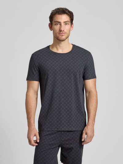 Männermodel trägt T-Shirt mit Logo-Muster und Rundhalsausschnitt von JOOP! Collection aus Baumwoll-Elasthan-Mix, Regular-Fit, Rückenlänge 68 cm, dunkle Farbe, glatte Textur, Ganzkörperansicht von vorne.
