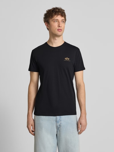 Männermodel trägt T-Shirt aus Baumwolle von Alpha Industries in Schwarz mit Label-Details, Gerader-Schnitt, Rundhalsausschnitt, Rückenlänge 67 cm, Ganzkörperansicht von vorne.