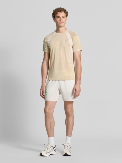 Męski model nosi Regular Fit T-Shirt mit Logo-Print Modell 'Road' von ASICS TIGER w jasnobeżowych i białych odcieniach, półprzejrzysty materiał, okrągły dekolt, długość tyłu w rozmiarze M: 69 cm, Ganzkörperansicht von vorne