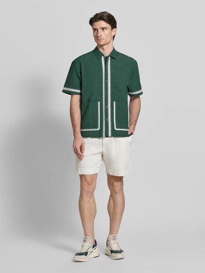 Mannenmodel draagt Regular Fit Freizeithemd mit aufgesetzten Taschen van WOODBIRD in groen met witte stiksels, korte mouwen, knoopsluiting, opgestikte zakken, kentkraag, volledige lichaamsweergave van voren