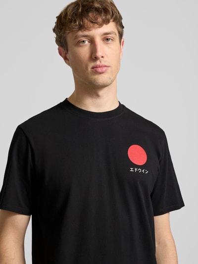 Męski model nosi czarne T-Shirt aus reiner Baumwolle Modell 'JAPANESE SUN' od Edwin z czerwonym nadrukiem z przodu, prosty krój, okrągły dekolt, kontekst: męska koszulka z bawełny, długość tyłu w rozmiarze M: 67 cm; zbliżenie górnej części ciała.