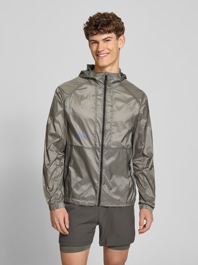 Männermodel trägt glänzende, graue Herren Jacke mit Kapuze, Reißverschluss und Reißverschlusstaschen, Modell 'SABER JACKET 2.0' von HALO, Regular-Fit, Logo auf der Brust, glatte Textur, Ganzkörperansicht von vorne.