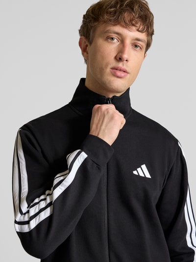 Männermodel trägt Regular Fit Sweat-Anzug aus Baumwoll-Mix von adidas Sportswear in Schwarz mit Optik: Unifarben, Nahaufnahme Oberkörper.