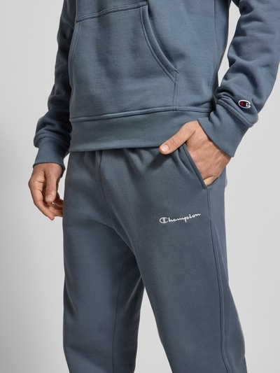 Mężczyzna nosi Straight Fit Sweatpants mit Label-Stitching od CHAMPION, mieszanka bawełny, elastyczny pas, wyhaftowane logo, zbliżenie na biodra.