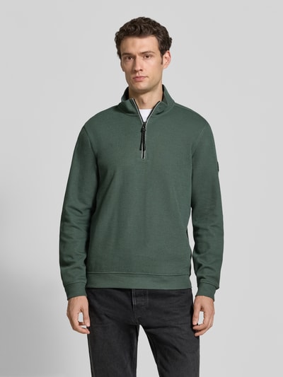 Männermodel trägt Relaxed Fit Sweatshirt aus Baumwoll-Mix Modell 'SELANIK' von LERROS in Dunkelgrün mit Troyer-Kragen, Ganzkörperansicht von vorne. Rückenlänge 68 cm, Ärmellänge 65 cm, elastische Abschlüsse.