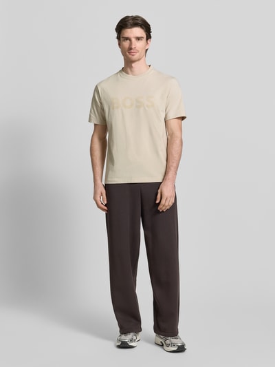 Männermodel trägt Regular Fit T-Shirt aus Baumwoll-Mix Modell 'ICONIC' von BOSS Green in Beige, unifarben, Label-Prägung, Ganzkörperansicht von vorne.