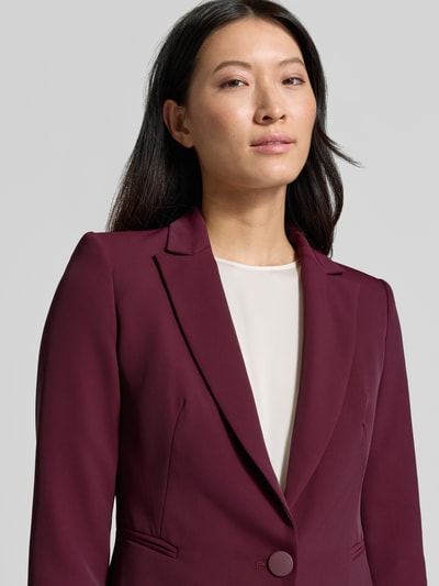 Vrouwenmodel draagt Slim Fit Blazer met reverskraag van Rinascimento in bordeaux met knoopsluiting en paspelzakken, detailopname bovenlichaam.