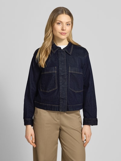 Kobiece model prezentuje Regular Fit Jeansjacke aus Baumwoll-Mix von Tom Tailor, ciemny denim, duże kieszenie, wyhaftowany motyw, wykładany kołnierz, listwa z zatrzaskami, splot twill, mieszanka bawełny, krój regular fit, widok całej sylwetki z przodu.