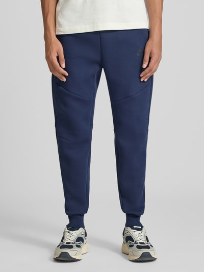 Mannenmodel draagt Slim Fit Sweathose uit katoenmix van Nike in donkerblauw met lichte sneakers, Heren Sweathose, detailopname onderlichaam