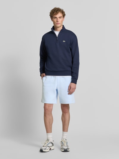 Männermodel trägt hellblaue Relaxed Fit Sweatshorts aus Baumwoll-Mix von Lacoste, lockere Passform, glatte Textur, Ganzkörperansicht von vorne. Herren Sweatshorts von Lacoste.
