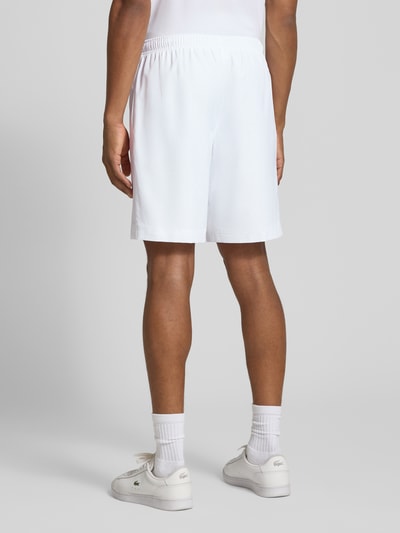 Männermodel trägt Relaxed Fit Shorts mit Logo-Patch von Lacoste in Weiß, glatte Textur, Herren Sportshorts von Lacoste Sport, Ganzkörperansicht Rückansicht.