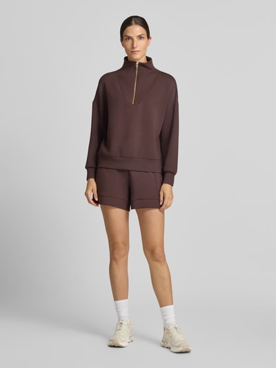 Frauenmodel trägt Regular Fit Sweatshirt aus Viskose-Mix Modell 'Hawley' von VARLEY in Braun mit Troyer-Kragen, elastischen Abschlüssen, Ganzkörperansicht von vorne.