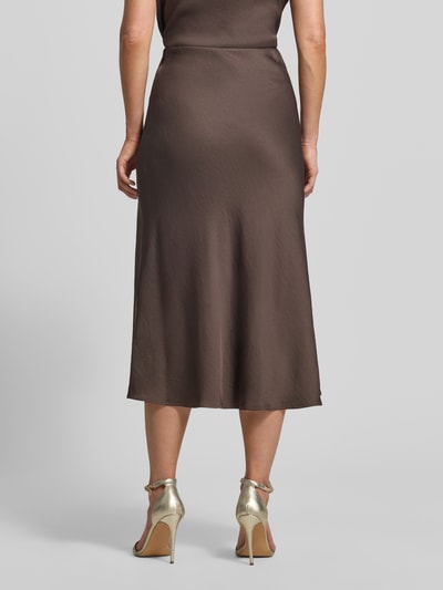 Frauenmodel trägt Midirock aus Satin Modell 'URA' von DRYKORN in Braun, leichte A-Linie, glatte Textur, Ganzkörperansicht Rückansicht. Damen Midirock von DRYKORN, Satin, A-Linie, elastischer Bund, Bundweite 34 cm, Länge 86 cm.