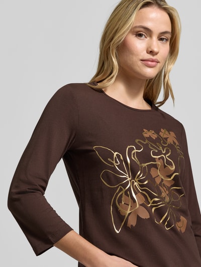 Frauenmodel trägt 3/4-Shirt mit Frontprint von TOM TAILOR in Braun mit goldfarbenem Motiv-Print, Regular Fit, 3/4-Arm, Nahaufnahme Oberkörper.
