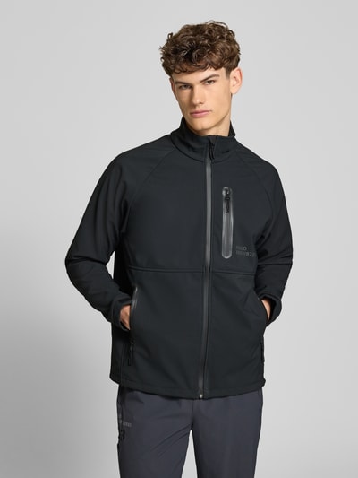 Männermodel trägt schwarze Softshell-Jacke mit Reißverschlusstaschen Modell 'ELITE' von HALO, Regular-Fit, Stehkragen, Label-Print, Ganzkörperansicht von vorne. Rückenlänge bei Größe M: 71 cm, Schulterbreite: 55 cm, Brustweite: 60 cm, Ärmellänge: 63 cm.