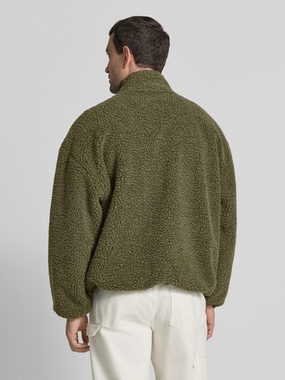 Männermodel trägt fleecejack met opstaande kraag, model 'HOKTOWN' van American Vintage met labeldetail, relaxed fit, olijfgroen, structuur met grove textuur, steekzakken, ritssluiting, ruglengte maat M/L 69 cm, schouderbreedte 56 cm, borstwijdte 48 cm, mouwlengte 55 cm, ganzendansicht rückansicht.