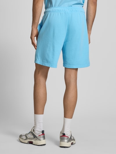 Männermodel trägt Sweatshorts mit Logo und elastischem Bund von CHAMPION in Hellblau, Baumwoll-Mix, Regular Fit, Rückansicht Ganzkörperansicht.