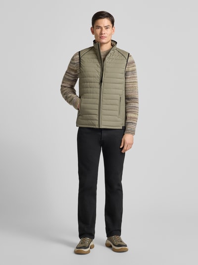 Männermodel trägt Steppweste mit Stehkragen und Reißverschlusstaschen von NAUTGÅRD, Regular-Fit, olivgrün, Ganzkörperansicht von vorne. Rückenlänge bei Größe M: 70 cm, Schulterbreite: 34 cm, Brustweite: 45 cm.