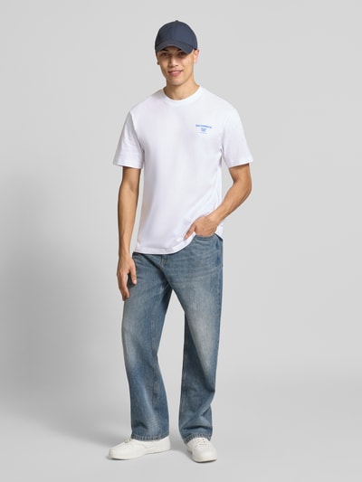 Mężczyzna model nosi Relaxed Fit T-Shirt aus reiner Bio-Baumwolle Modell 'FRED' von Only & Sons, biała koszulka z nadrukiem, jeansy, jasne kolory, jednolita struktura materiału, całopostaciowy widok z przodu.