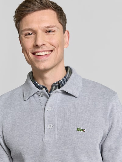 Mężczyzna model nosi Regular Fit Sweatshirt aus reiner Baumwolle od Lacoste, szara melanż, logo, kołnierzyk polo, długi rękaw, dzianina bawełniana, zbliżenie górnej części ciała.