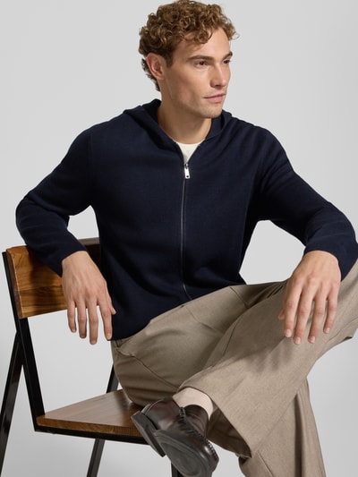 Männermodel trägt Regular Fit Strickjacke mit Lanawoll-Anteil von Christian Berg Men in Dunkelblau, Zipper und Kapuze, Nahaufnahme Oberkörper, Material-Mix.