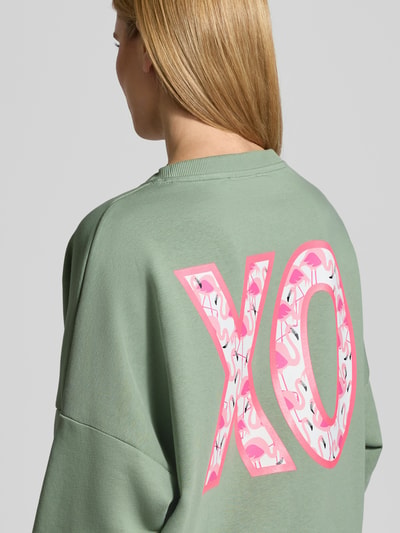 Frauenmodel trägt Relaxed Fit Sweatshirt mit Pailettenbesatz Modell 'XO' von miss goodlife in Grün und Rosa, Baumwolle, Rückansicht Nahaufnahme.