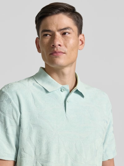 Männermodel trägt Regular Fit Poloshirt aus Baumwoll-Mix Modell 'PE_FLOWER' von BOSS Orange in Hellgrün mit Struktur, Nahaufnahme Oberkörper.