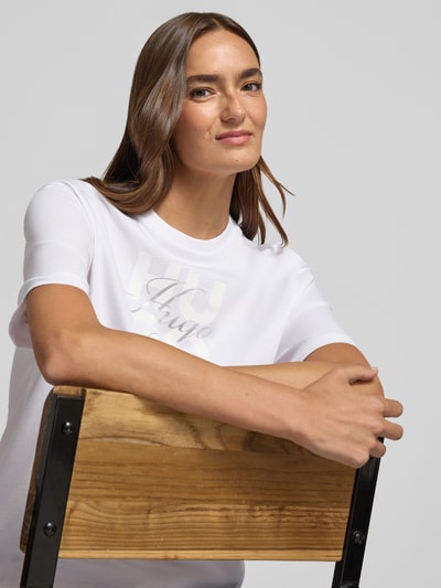 Kobiece model prezentuje damski t-shirt Regular Fit T-Shirt aus reiner Baumwolle Modell 'Dashire_5' od HUGO, biały, gładki materiał, z przodu nadruk, półzbliżenie górnej części ciała, damski t-shirt od HUGO.