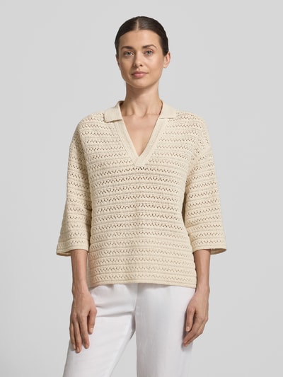 Modelka kobieca ma na sobie sweter z dzianiny z dekoltem w serek i rękawem o dł. 3/4 model 'Garakino' od OPUS, z czystej bawełny, krój relaxed fit, kołnierzyk polo, długość tyłu w rozmiarze 36: 56 cm, długość rękawów w rozmiarze 36: 33 cm, kremowy kolor, widoczne ażurowe faktury, całkowity widok od przodu.