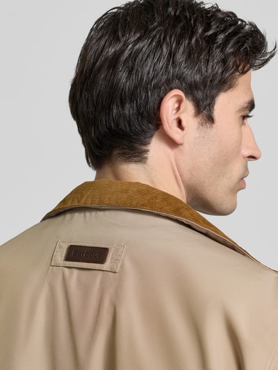 Männermodel trägt Regular Fit Hemdjacke mit Stehkragen van Barbour, look: effen, labelpatch en labelopschrift, detailaufnahme schouder en kraag, context: heren, pasvorm regular fit, kraagmodel opstaande kraag, motief binnenkant geruit, mouwvorm lange mouw, ritssluiting, ritszakken, klepzakken, binnenzak.