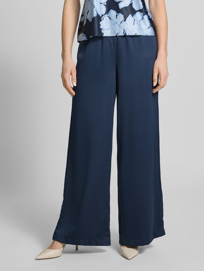 Vrouwenmodel draagt Loose Fit Pants mit elastischem Bund und Eingrifftaschen van Christian Berg Cocktail in marineblauw, los vallende snit, elastische taille, Franse steekzakken, achterzakken met paspel, gladde textuur, vooraanzicht hele lichaam.