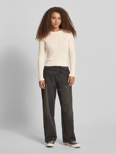 Frauenmodel trägt Strickpullover mit Zopfmuster und Label-Stitching von REVIEW, cremefarben, Baumwoll-Mix, Regular-Fit, Rundhalsausschnitt, Ganzkörperansicht von vorne.