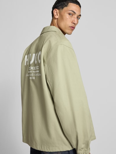 Männermodel trägt Regular Fit Bomberjacke / Blouson aus reiner Baumwolle Modell 'Biyo2631' von HUGO Blue, sandfarben, Rückansicht.