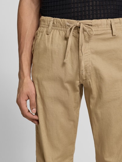 Männermodel trägt Relaxed Fit Hose aus Baumwoll-Leinen-Mix Modell 'KANE' von Jack & Jones, beige Farbe, Schnürung, Nahaufnahme Oberkörper, Kontext: Herren Hose, elastischer Bund, Gesäßtaschen, Bundweite 42 cm, Innenbeinlänge 82 cm.
