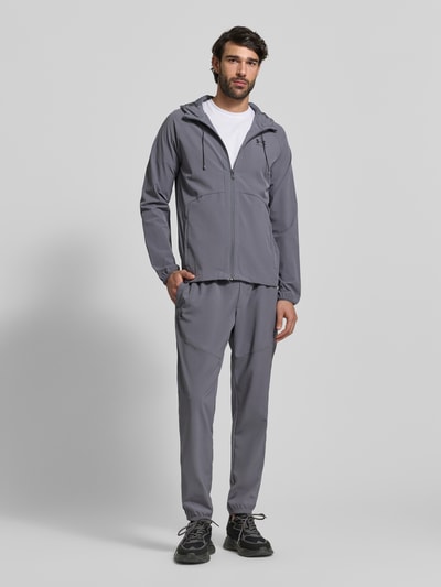 Männermodel trägt Regular Fit Jogger mit Logo-Print Modell 'Vibe' von Under Armour im grauen Elastischer-Material-Mix, Eingrifftaschen, elastischer Bund mit Tunnelzug, elastische Beinabschlüsse, Ganzkörperansicht von vorne.