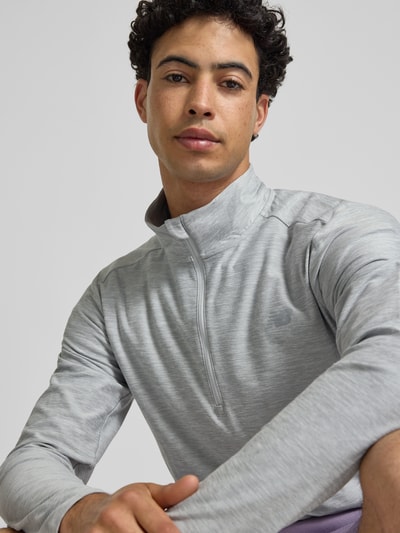 Männermodel trägt Regular Fit Sweatshirt mit Troyer-Kragen von New Balance in hellgrau, Logo-Print, elastischer Material-Mix, Nahaufnahme Oberkörper.